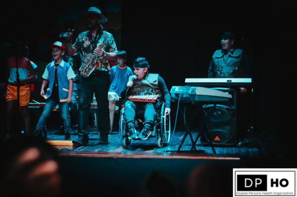 Diverse group of children performing on a stage, featuring a young boy in a wheelchair singing with a microphone, representing the evolving landscape and building an inclusive future for Special Education in China. This scene highlights the success of activity-based learning and the integration of students with disabilities into mainstream performing arts. Branded with the DP-HO Disable Persons Health Organization logo.