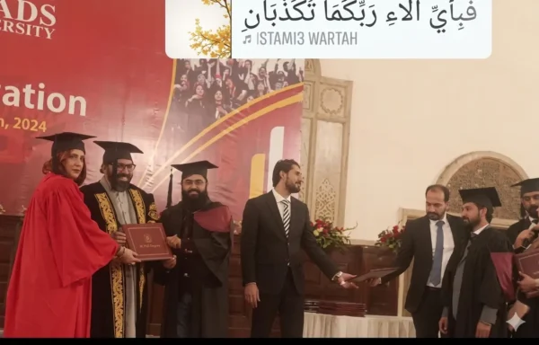 A high-quality photo of Imtiyaz Ali receiving his M.Phil degree certificate on stage during the graduation convocation ceremony at Lahore Leads University, Lahore. Imtiyaz Ali, dressed in a traditional black and maroon academic gown and cap, stands smiling as university officials in formal red and patterned regalia present him with his degree folder. An Islamic calligraphic banner featuring the verse "Fabi-ayyi ala-i rabbikuma tukadhdhiban" is displayed at the top.